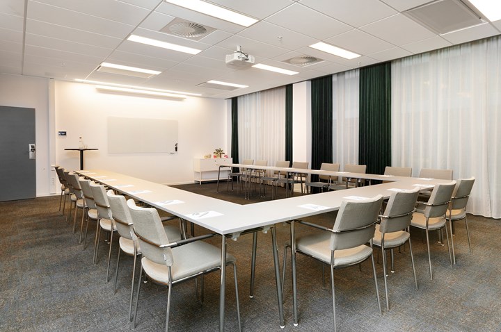 Conference room with u-shaped seating, white chairs, white table, gray carpet and draperies