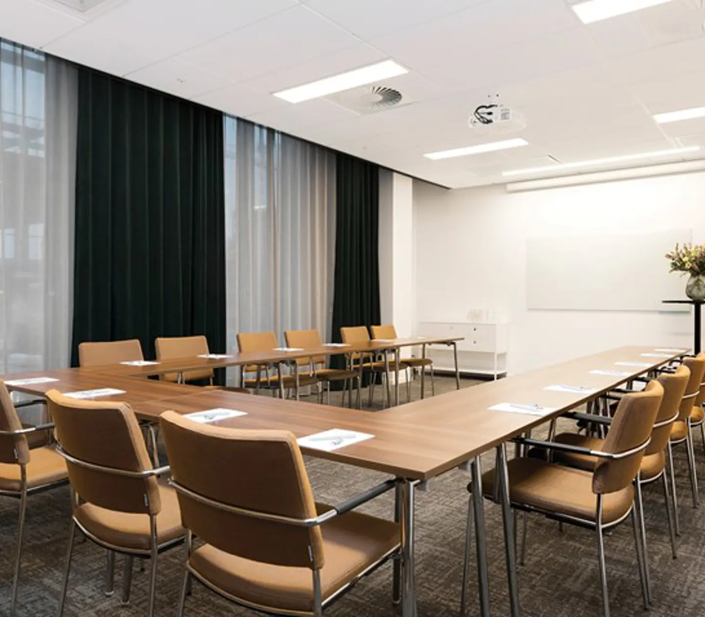 Konferensrum med u-sittning, bruna möbler, vita väggar, grå matta och stora fönster