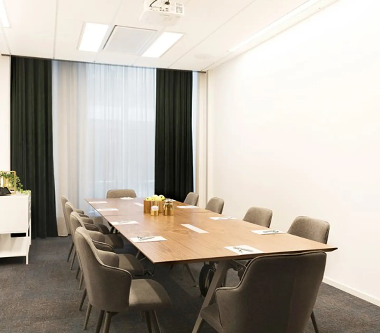 Konferensrum med styrelsesittning, vita väggar, grå matta