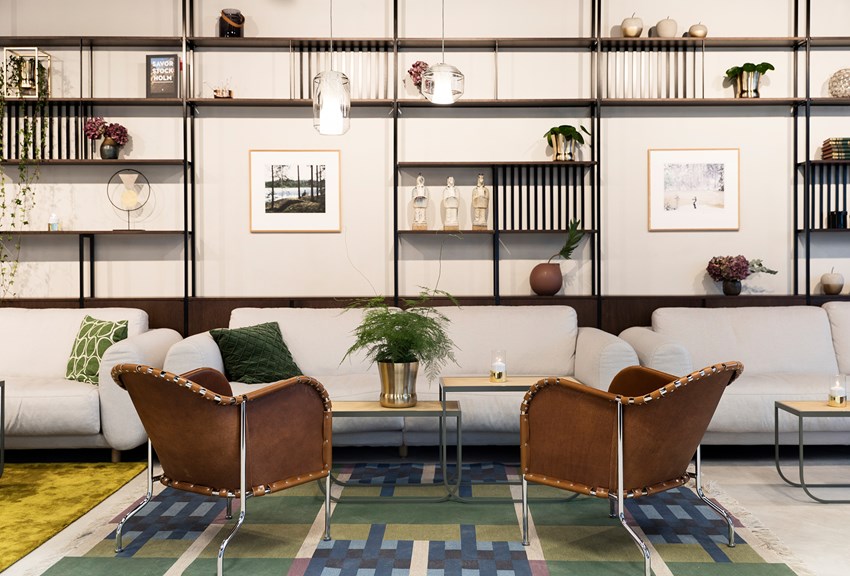 Modern inredningsdesign med vita soffor, bruna stolar och hyllor. Grön växt i mitten och konst på väggarna, skapar en elegant och inbjudande miljö.