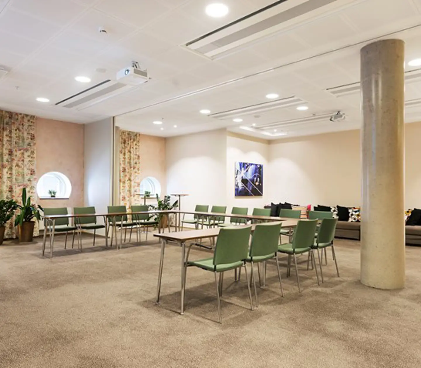 Konferensrum med u-sittning, ljusbrunt golv, gröna stolar och mönstrade draperier