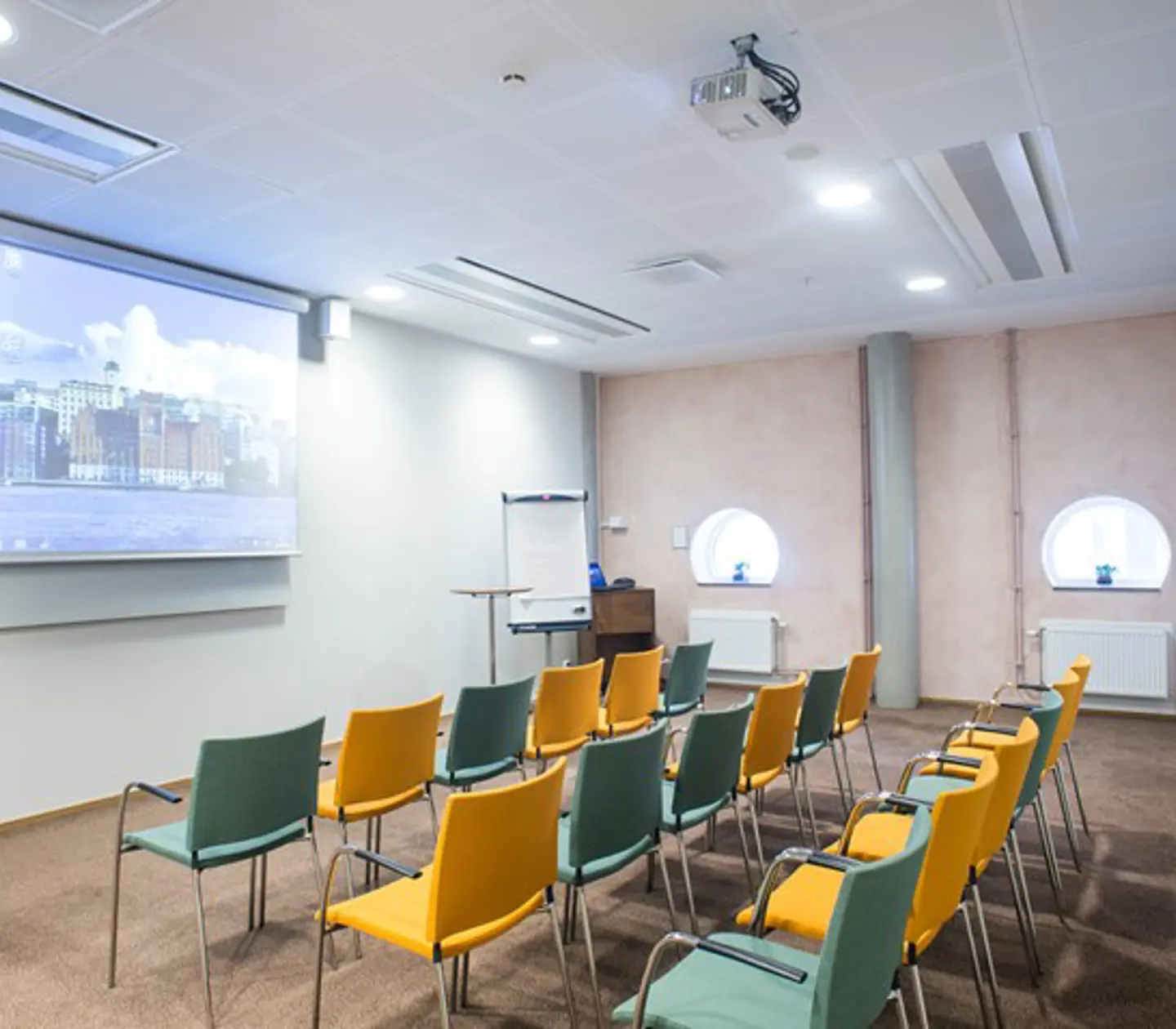 Konferensrum med biosittning, gula och blå stolar, vita väggar och projektor