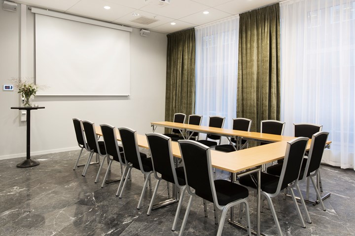 Konferensrum med u-sittning, träbord, svarta stolar och gröna gardiner