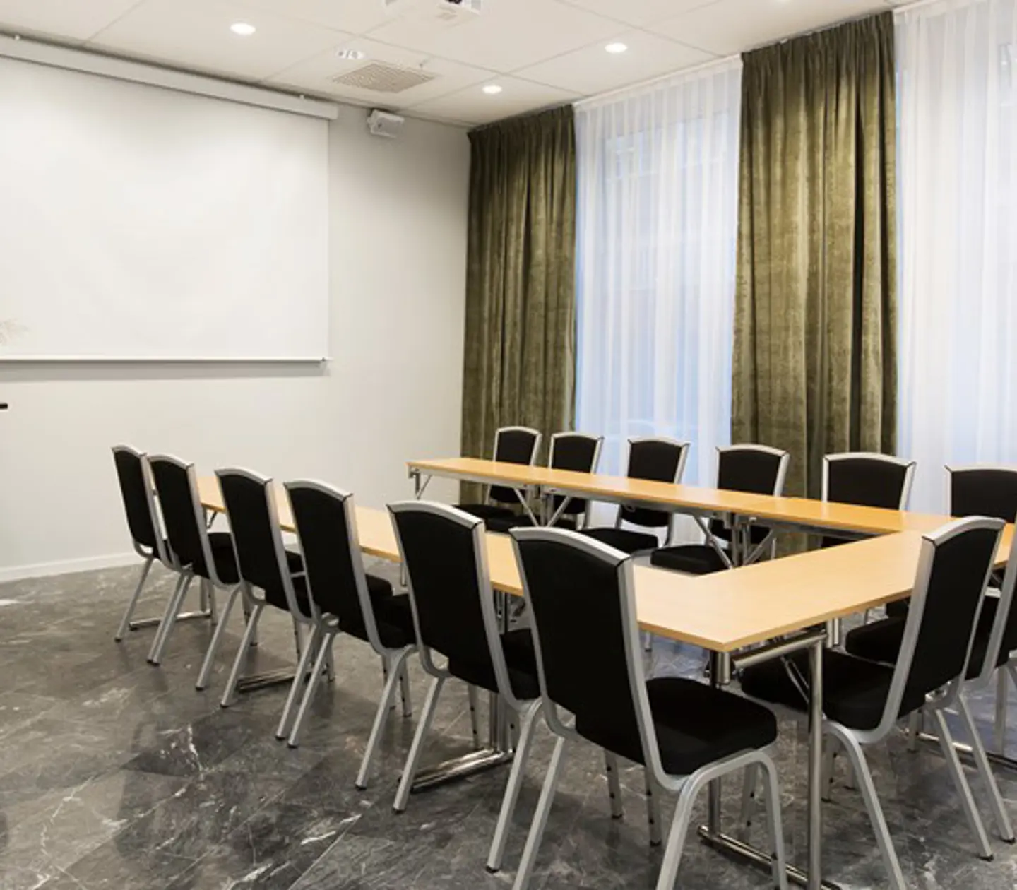 Conference room with u-shaped seating, wooden table, black chairs and green curtains