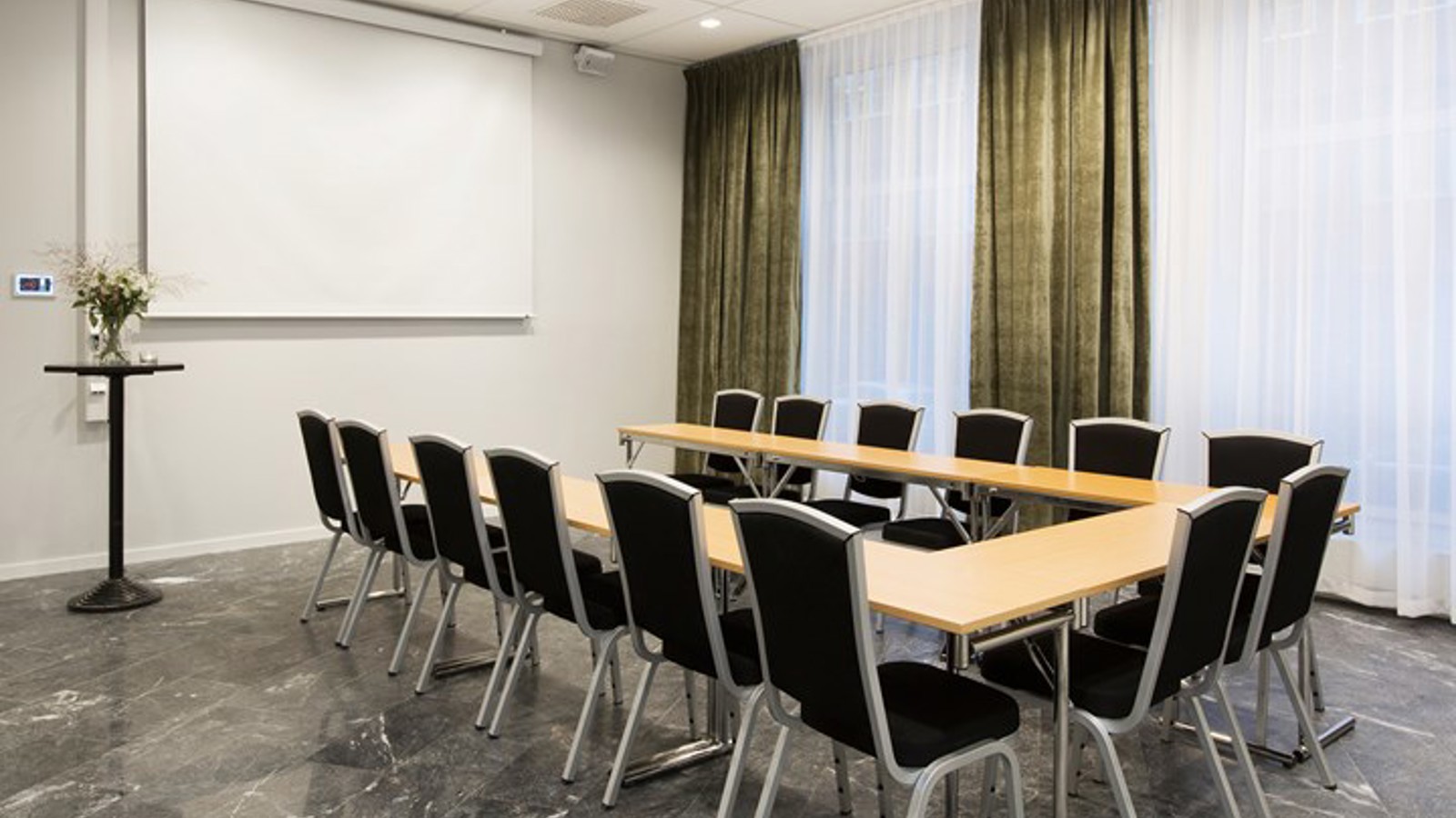 Conference room with u-shaped seating, wooden table, black chairs and green curtains