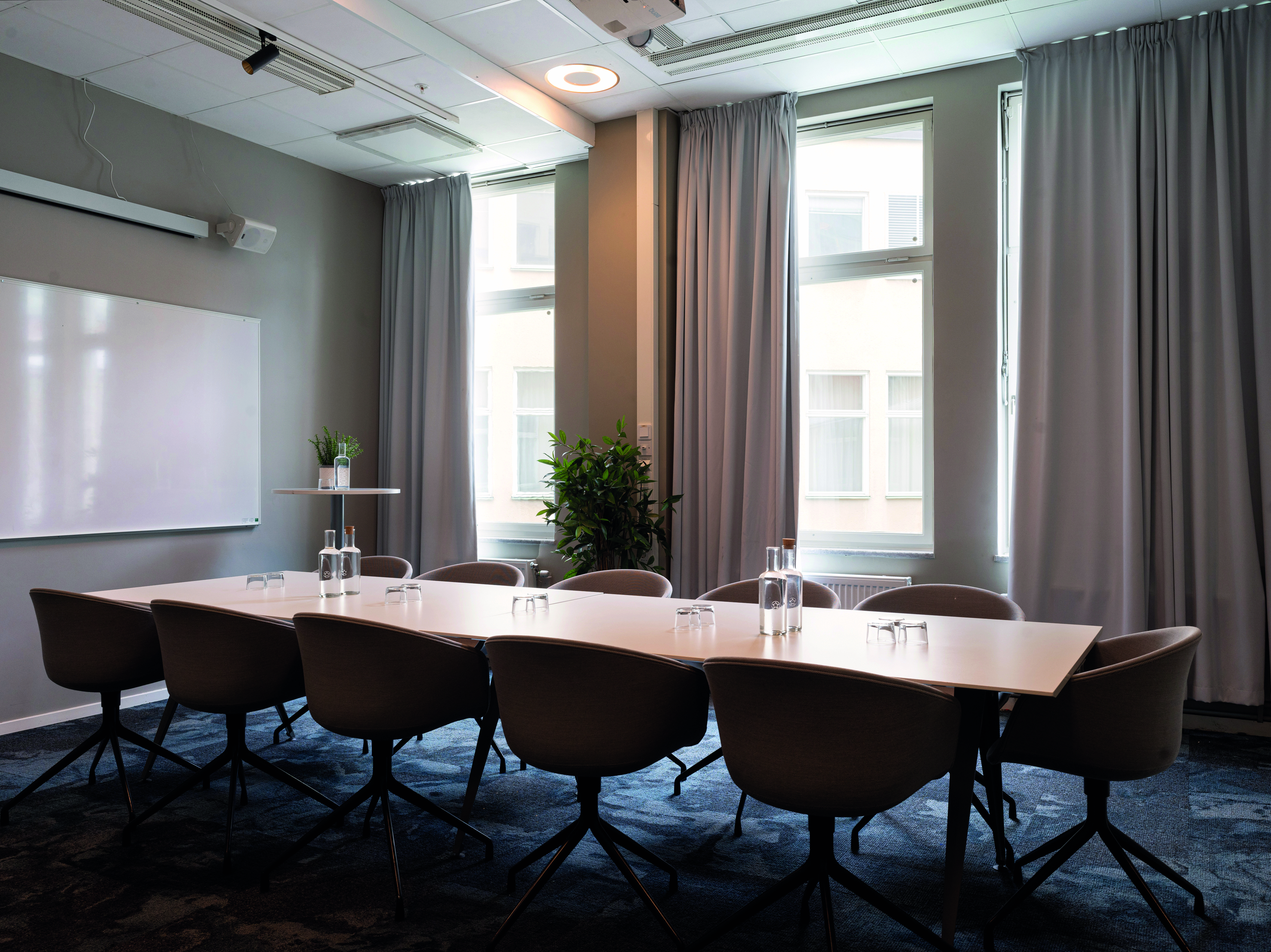 Konferensrum med skolsittning, stora fönster, träbord, blå matta