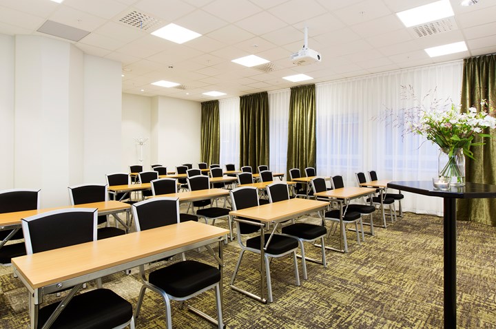 Konferensrum med skolsittning, vita väggar, svarta stolar, träbord