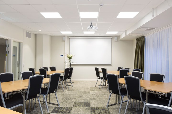 Konferensrum med ö-sittning, vita väggar, svarta stolar, träbord