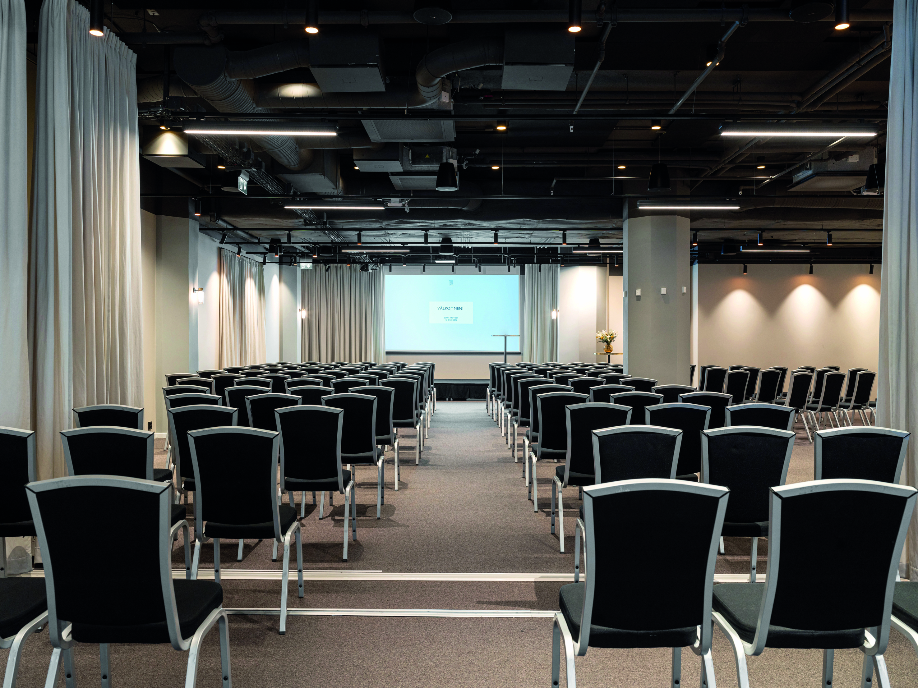 Konferensrum med bio-sittning, mörka stolar och vita väggar