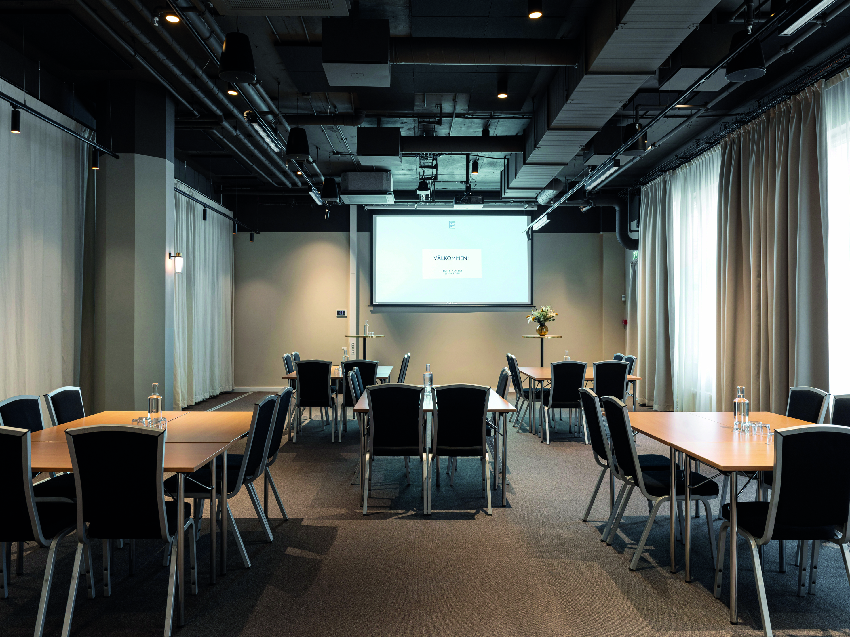 Konferensrum med u-sittning, vita väggar, mörkt golv, ljusa gardiner