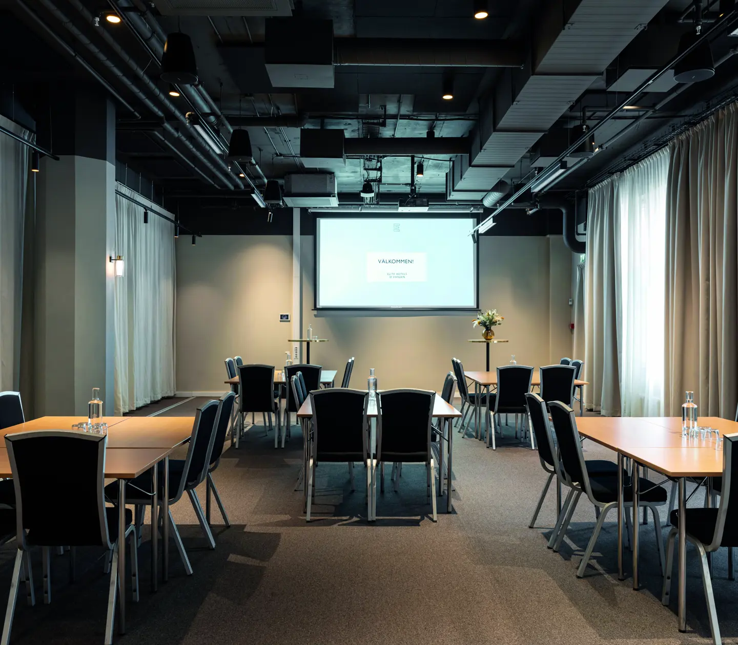 Conference room with u-shaped seating, white walls, dark floor, light curtains