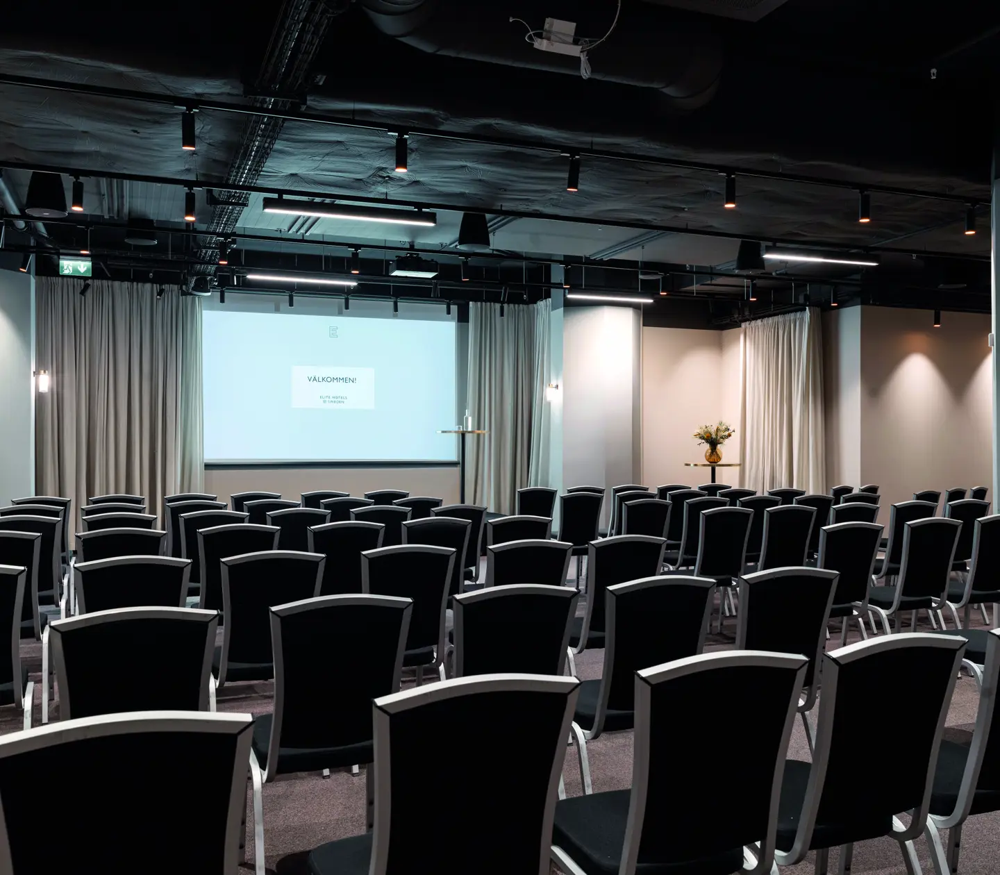 Konferensrum med biosittning, grå stolar, vita väggar och projektor