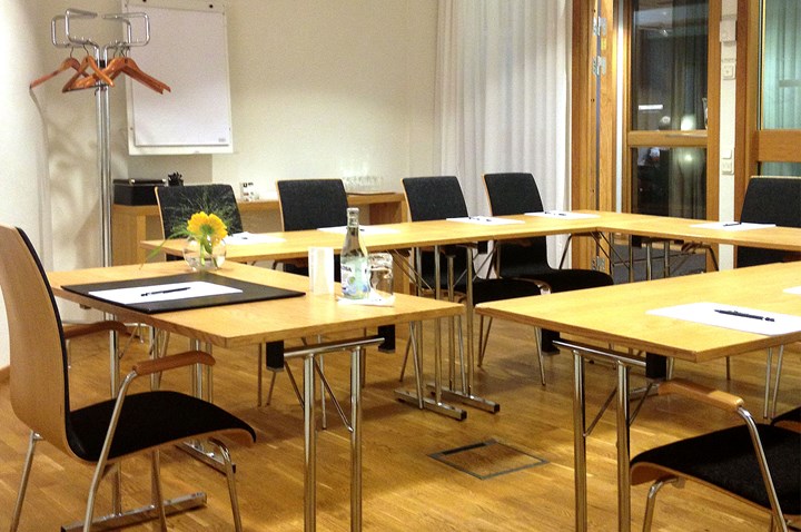 Konferensrum med vita väggar, trägolv och trämöbler i u-sittning