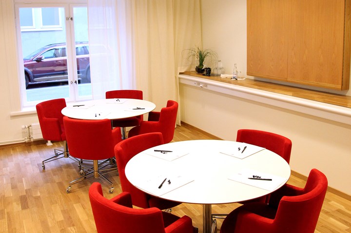 Ljust konferensrum med vita bord och röda stolar uppställda som öar