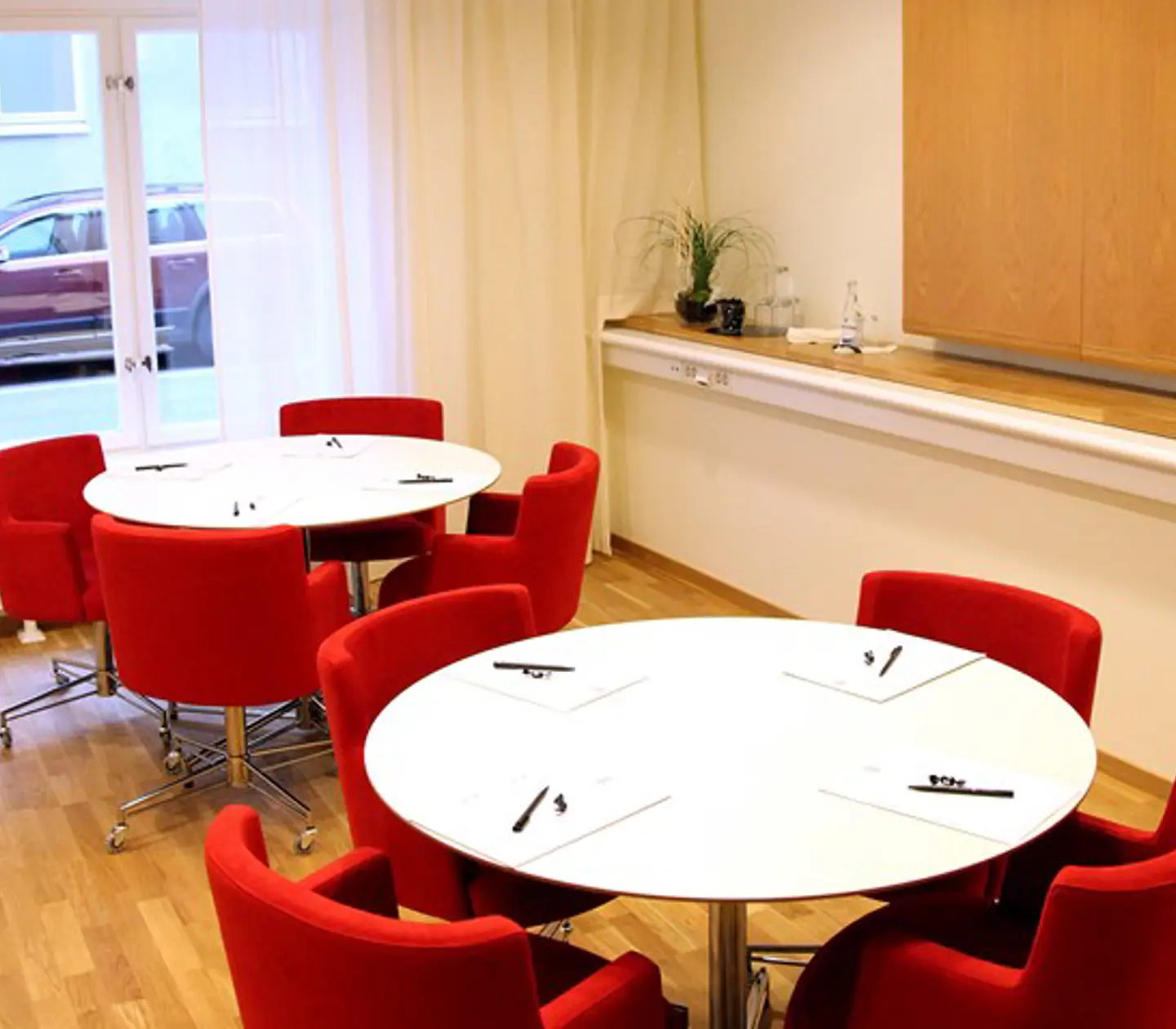 Bright conference room with white round tables and red chairs
