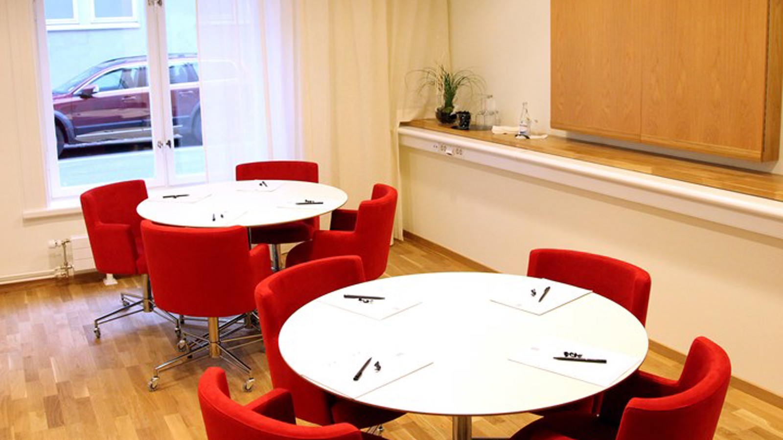 Bright conference room with white round tables and red chairs