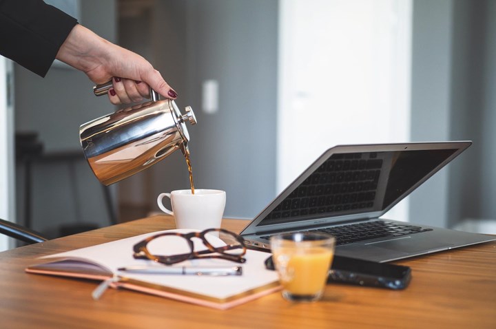 Close-up of hand pouring coffee, with open book and laptop in the foreground