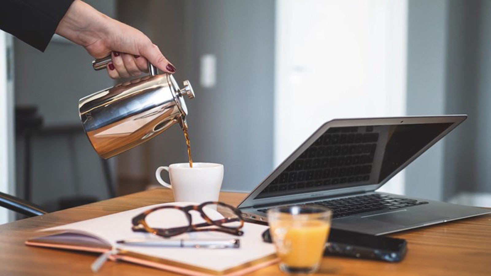 Close-up of hand pouring coffee, with open book and laptop in the foreground