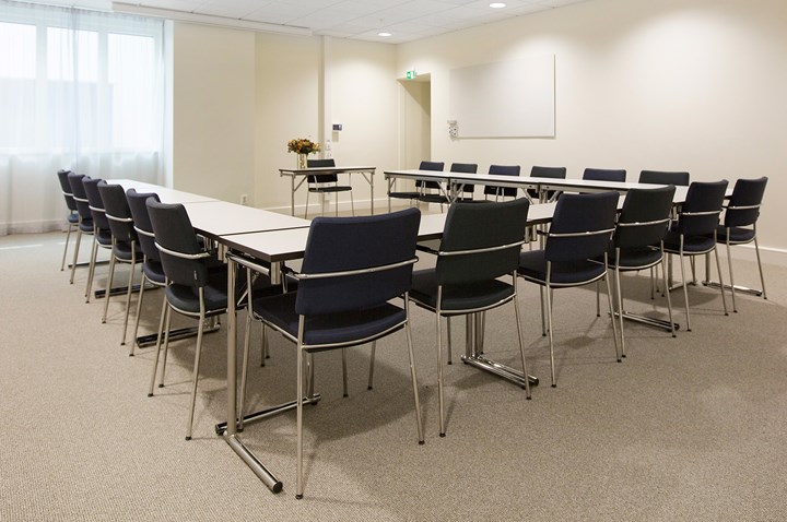 Bright conference room with u-shaped seating, white walls and black chairs