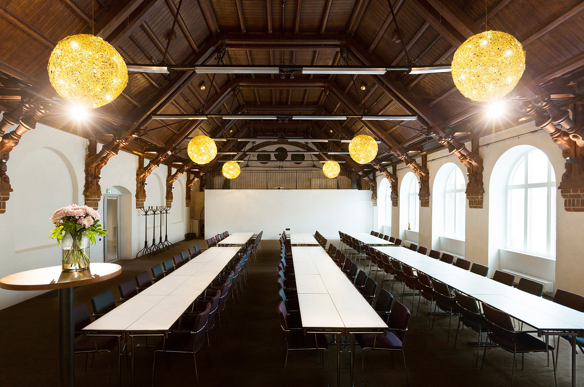 Large room with long white tables, dark chairs and high ceiling