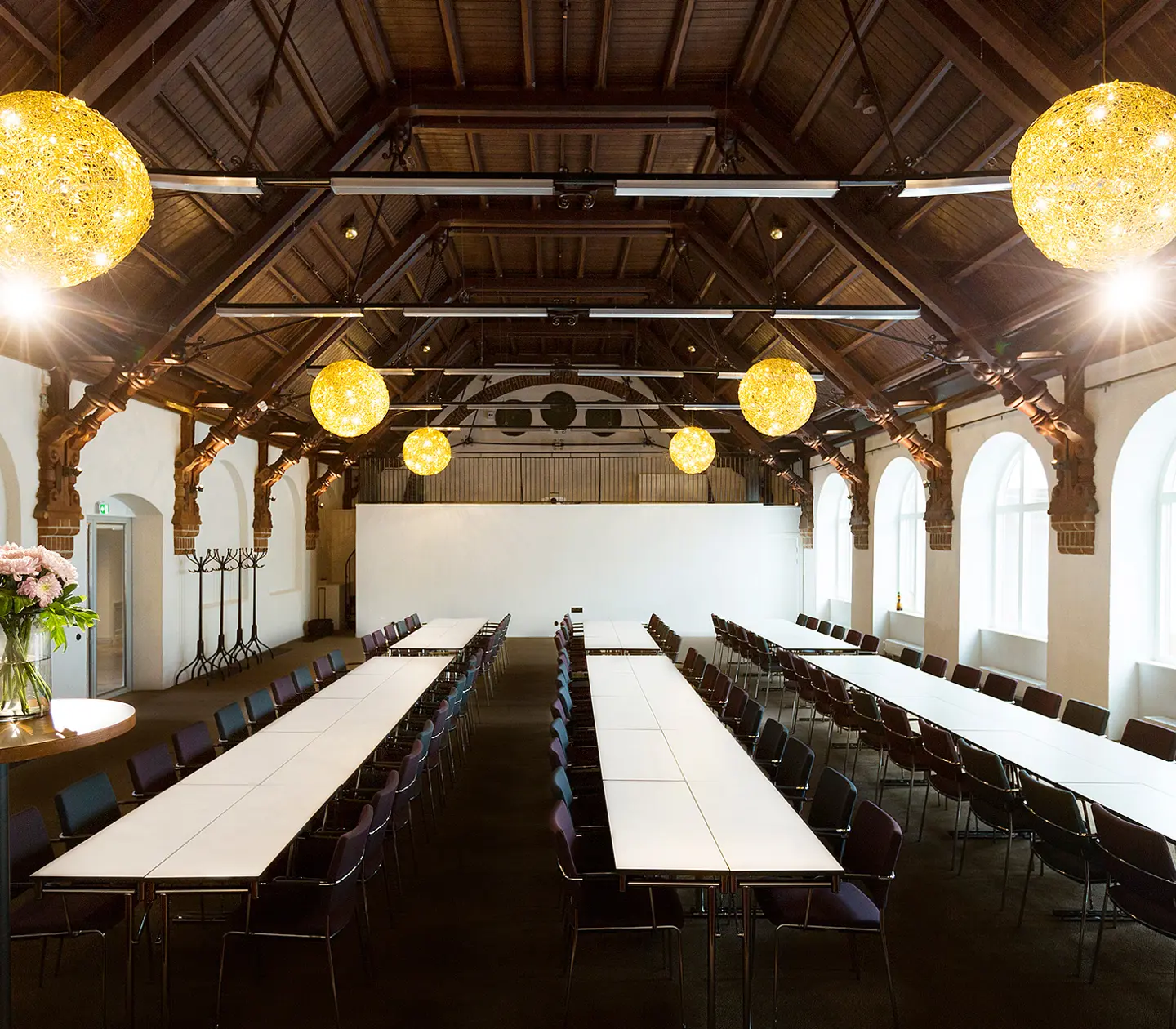 Large room with long white tables, dark chairs and high ceiling