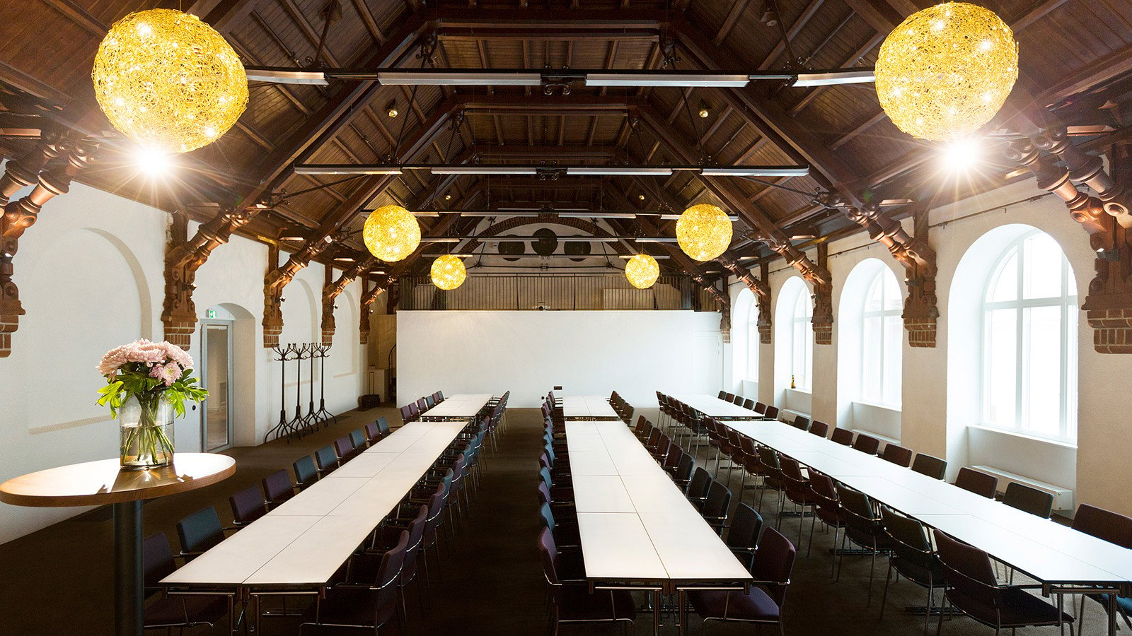 Large room with long white tables, dark chairs and high ceiling