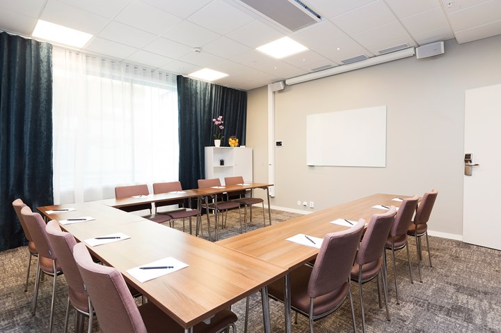 Konferensrum med u-sittning, träbord, ljusa väggar, mörka gardiner