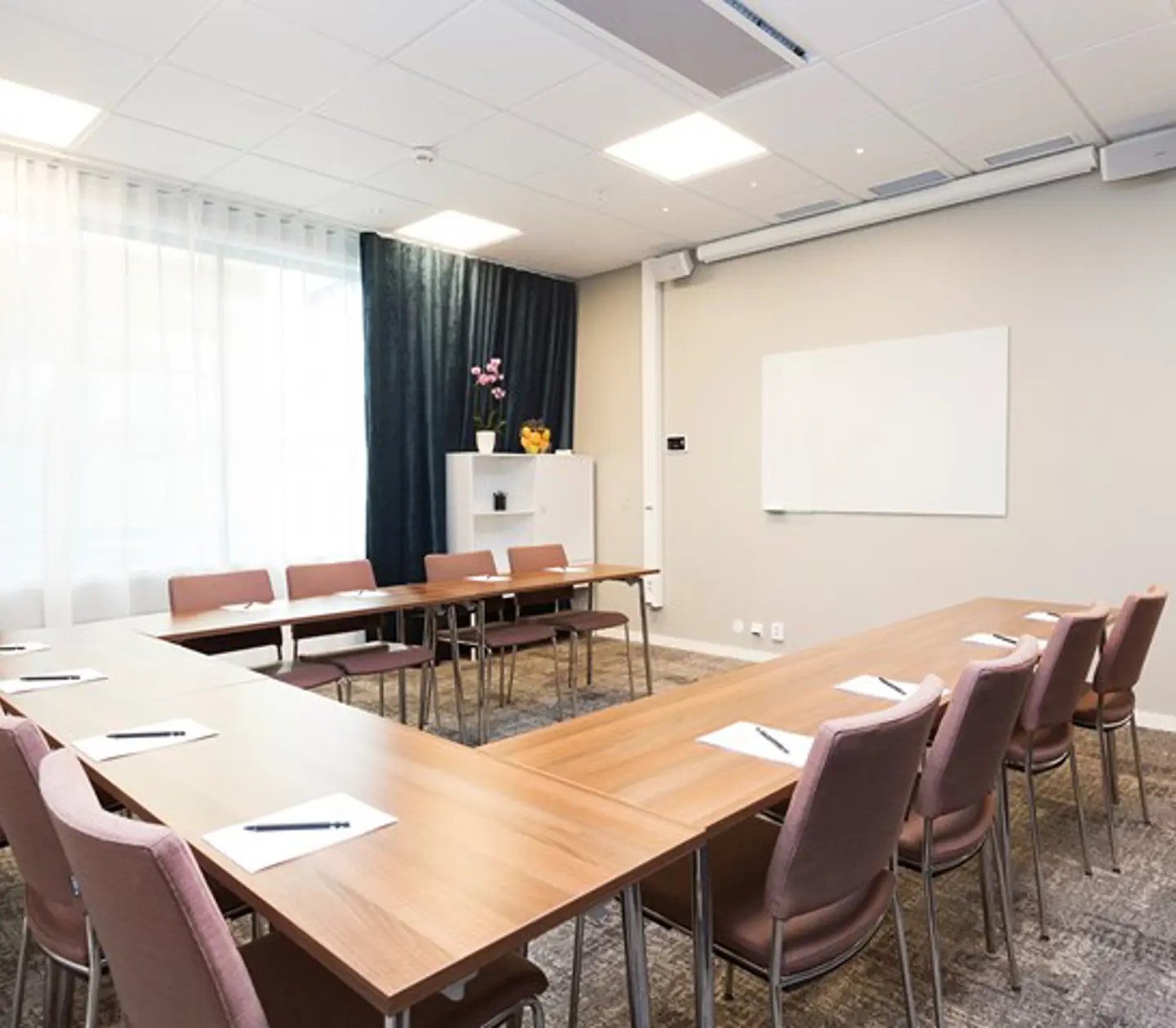 Konferensrum med u-sittning, träbord, ljusa väggar, mörka gardiner