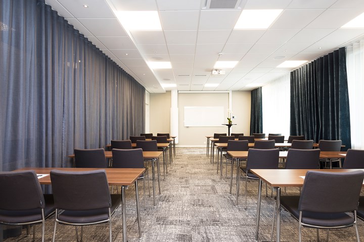 Konferensrum med skolsittning, grå stolar, grått golv och grå draperier