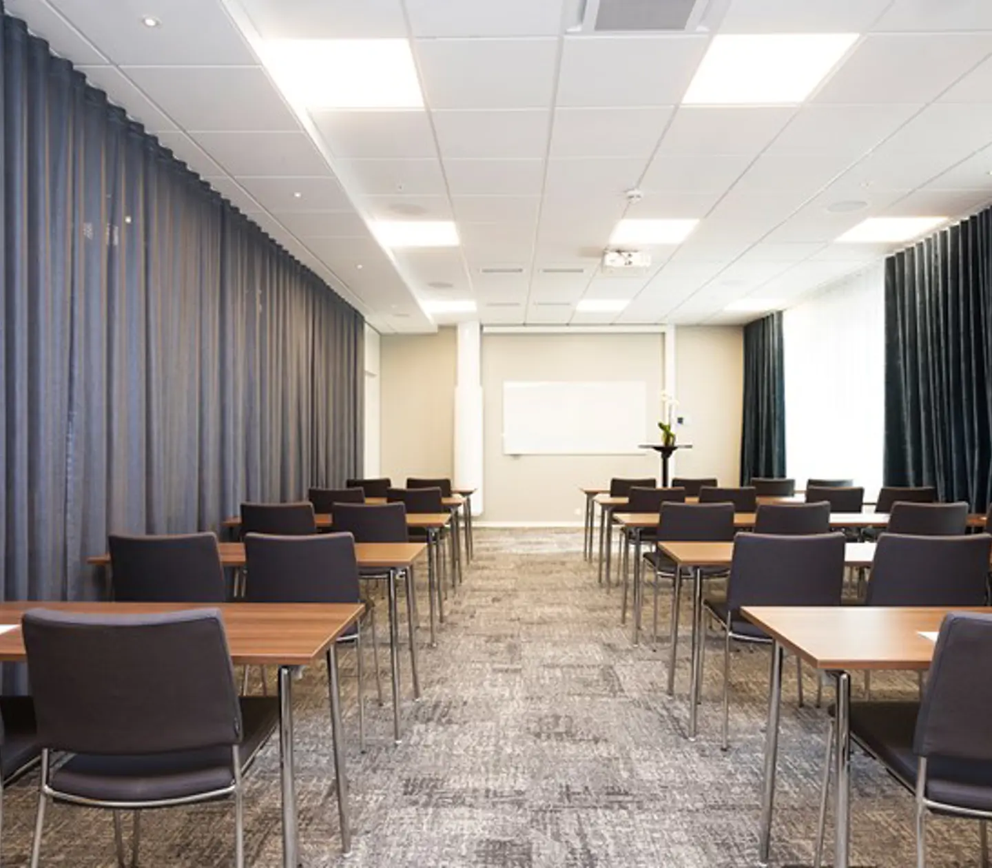 Konferensrum med skolsittning, grå stolar, grått golv och grå draperier