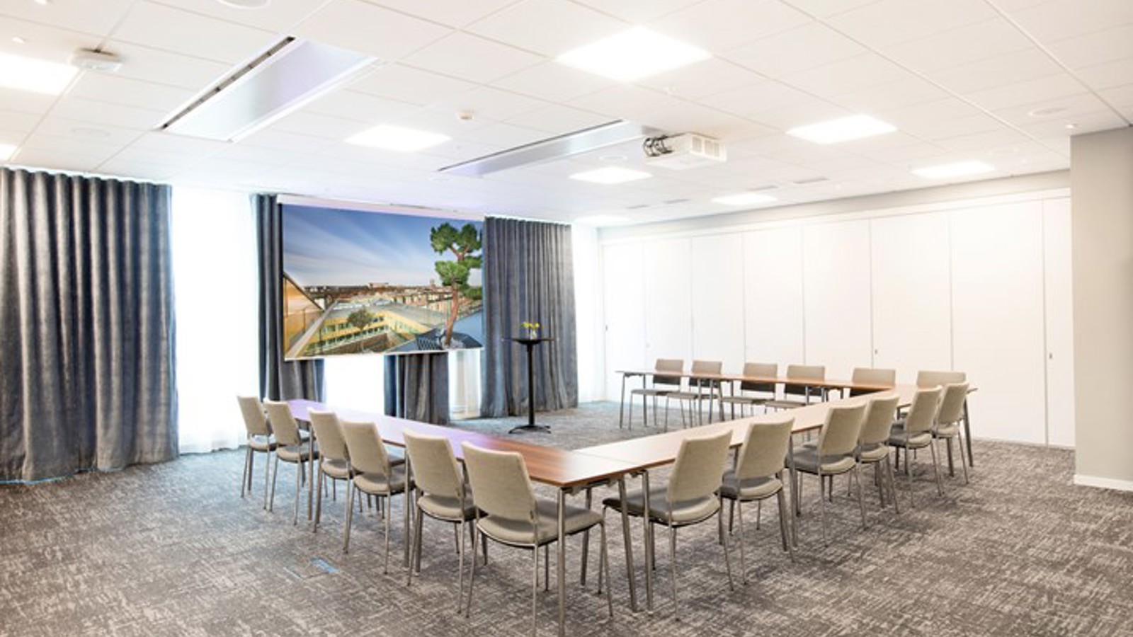 Conference room with U-shaped seating, gray floor, gray chairs and lit lights in the ceiling