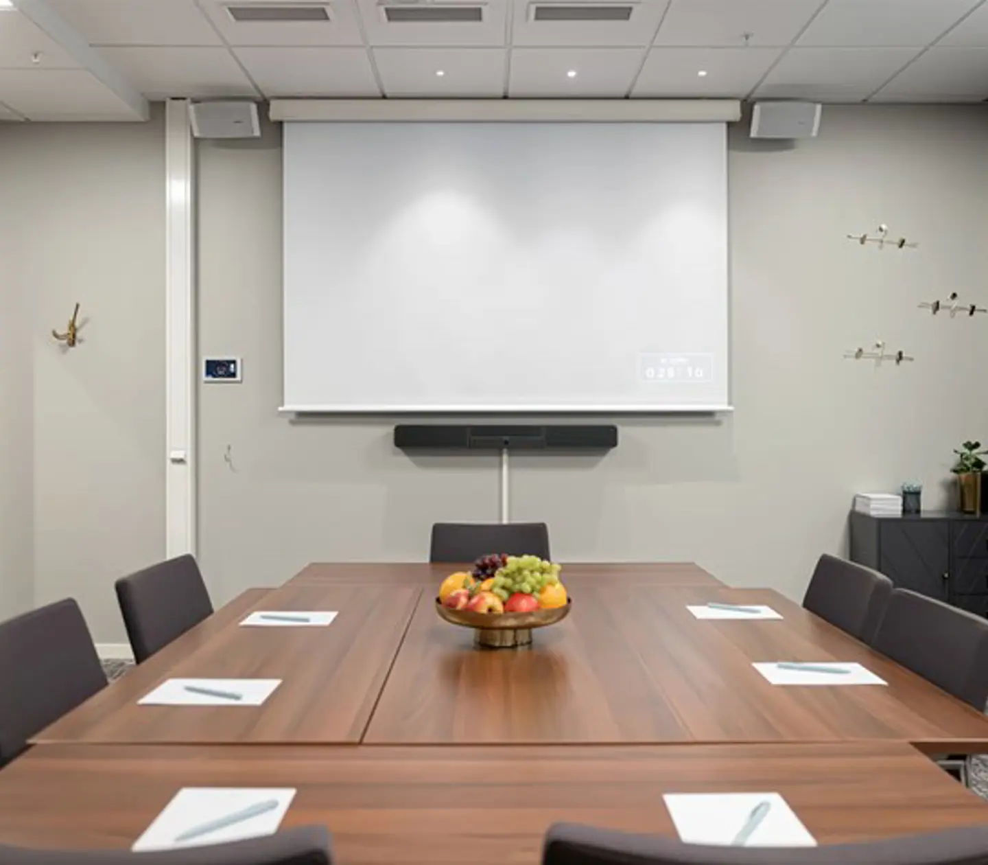 Konferensrum med brunt bord, grå stolar, ljusa väggar och projektor