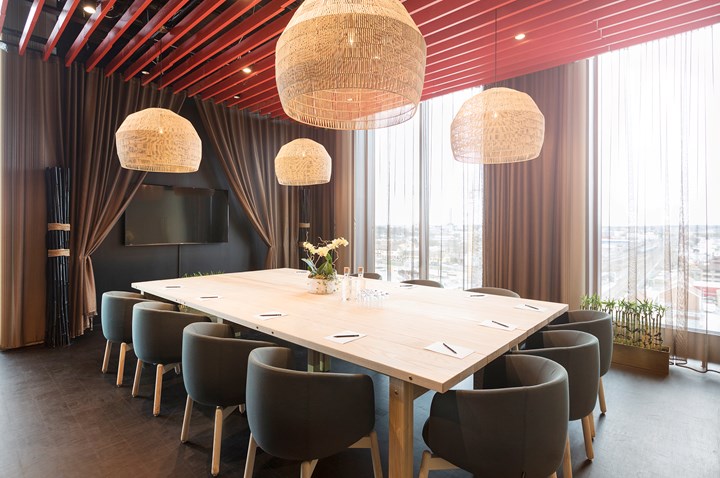 Konferensrum med styrelsesittning, stora fönster, röd panél i taket och bruna draperier