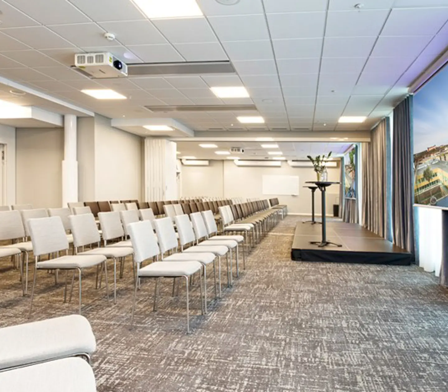 Konferensrum med biosittning, grått golv, vita stolar och vita väggar