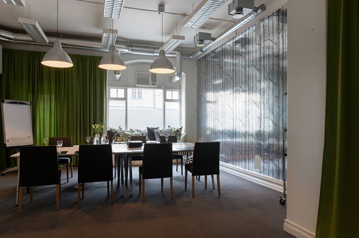 Konferensrum med styrelsesittning, mörka stolar och gröna drapperier