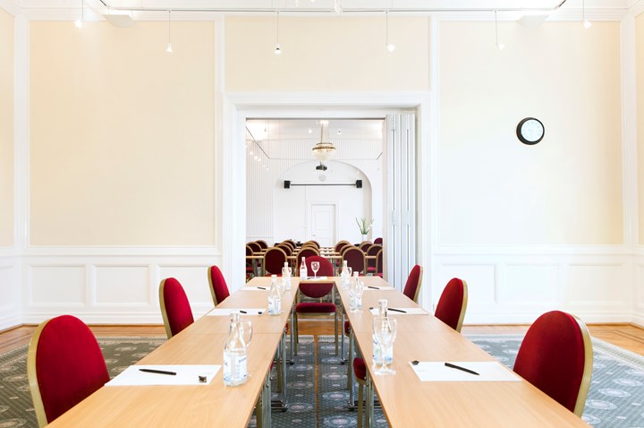 Konferensrum med u-sittning, träbord, röda stolar, ljusa väggar och grönmönstrad matta