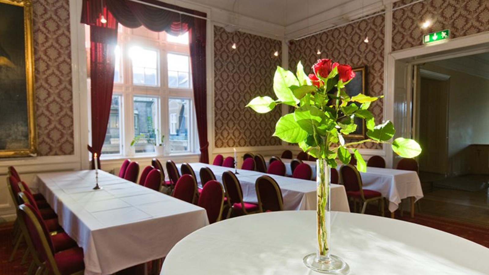 Room with set tables, white tablecloths and vase of roses