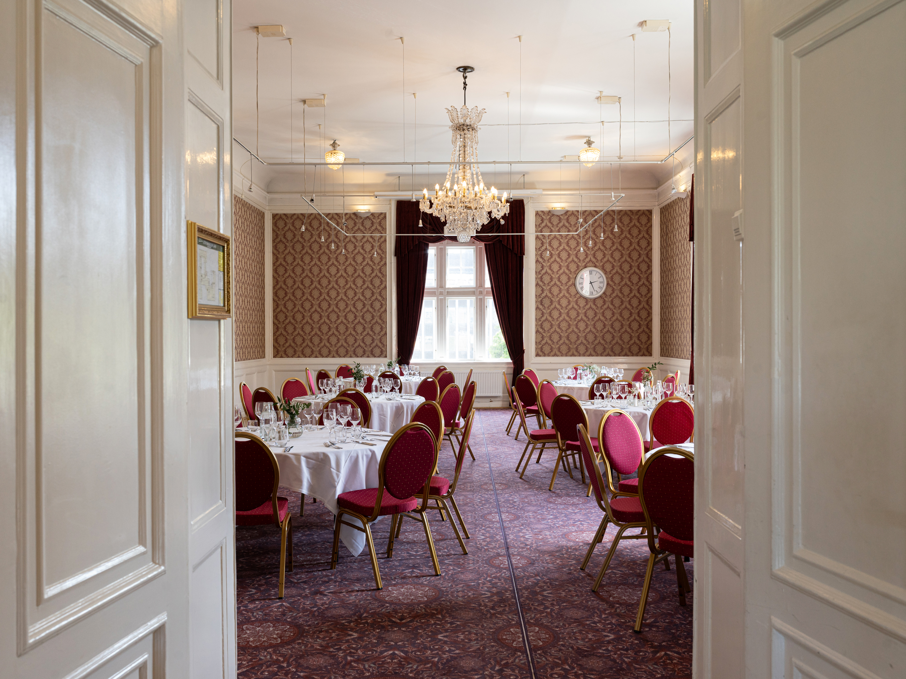 Elegant matsal med röda stolar och vita dukar, kristallkrona, och klassisk inredning.