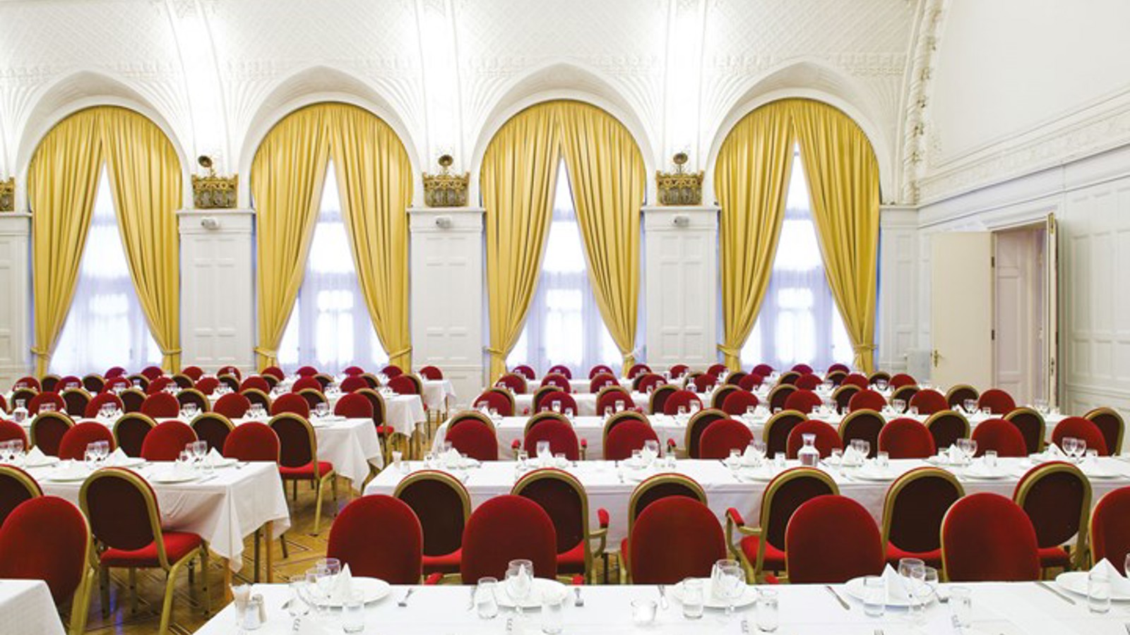 Large room with set tables, white tablecloths and red chairs