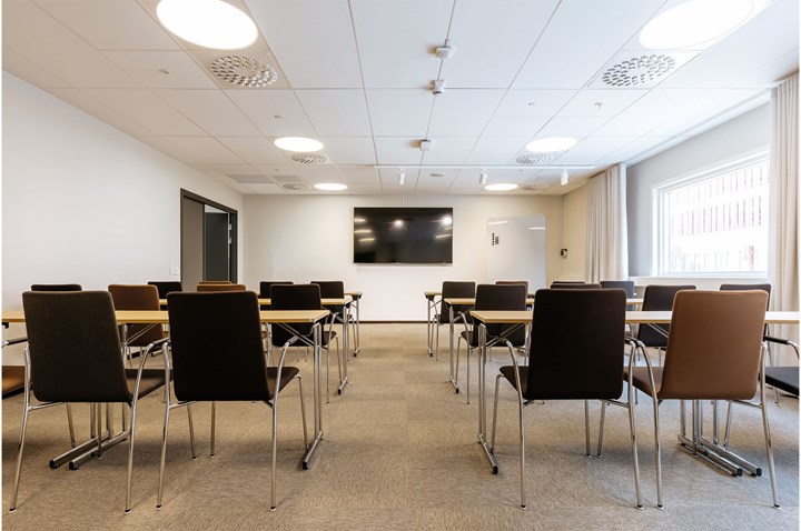 Konferensrum med skolsittning, vita väggar och brun matta