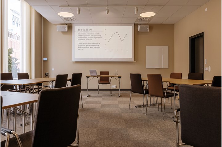 Konferensrum i ljusbruna toner, med bord och stolar i ö-sittning