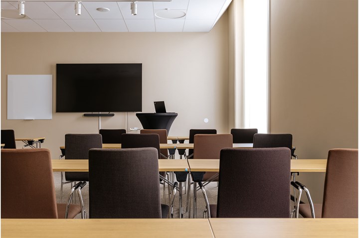 Konferensrum med skolsittning i ljus- och mörkbruna färger med tv-skärm och fönster