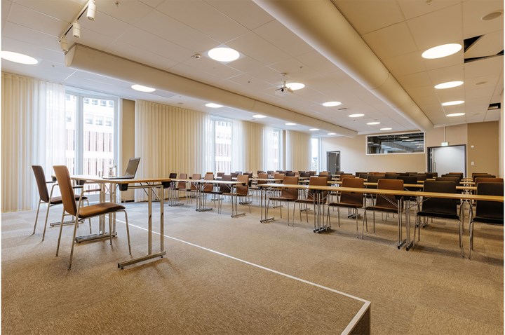 Konferenslokal i skolsittning, med scen och stora fönster