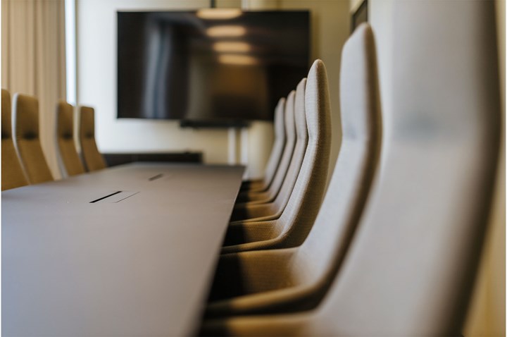 Närbild på långt konferensbord, stolar och tv-skärm