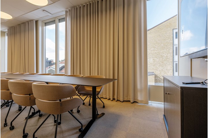 Konferensrum med styrelsesittning, stora fönster och draperier