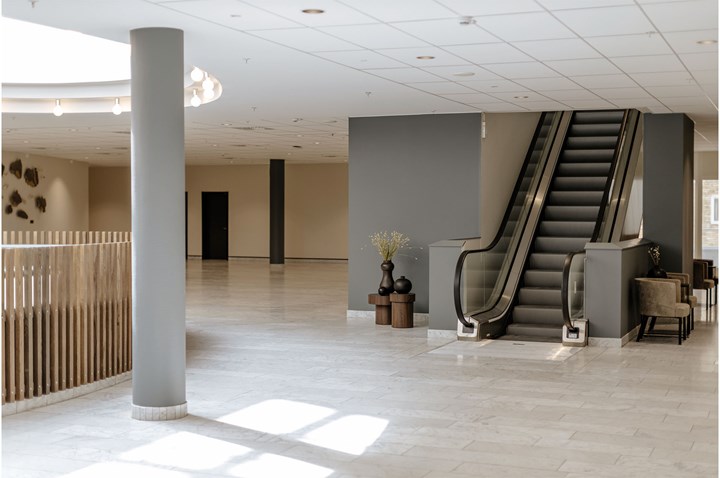 Öppen inomhusyta med stenlagt ljust golv, pelare, takfönster och rulltrappa