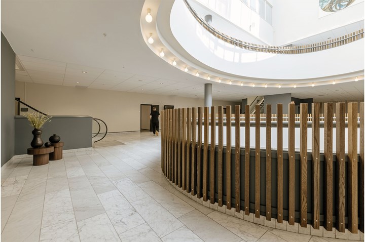 Öppen inomhusyta med träpanél, ljust stengolv, runt takfönster och rulltrappa