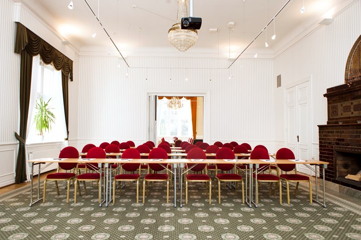 Konferensrum med skolsittning, röda stolar, vita väggar och grönmönstrad matta