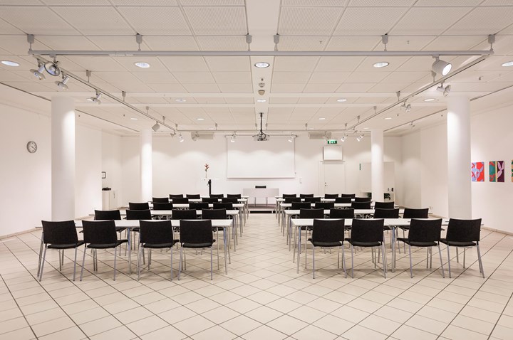 Conference room with white walls, white floor and black chairs placed in cinema seating