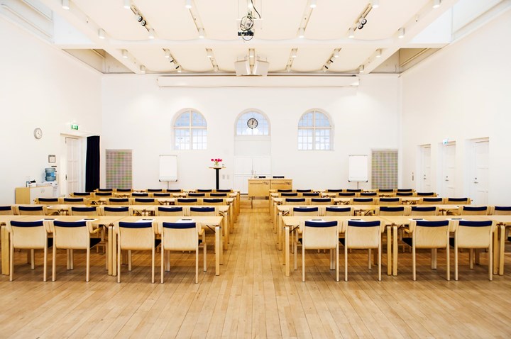 Conference with cinema seating, wooden chairs, wooden floor and white walls